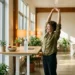 Professional stretcht energiek naast een staand bureau met waterles en fruit in zonnig, modern Nederlands kantoor.