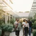 Diverse medewerkers lopen samen door een zonnig modern kantoorkwartier, één draagt een yogamat, een ander houdt fruit vast.